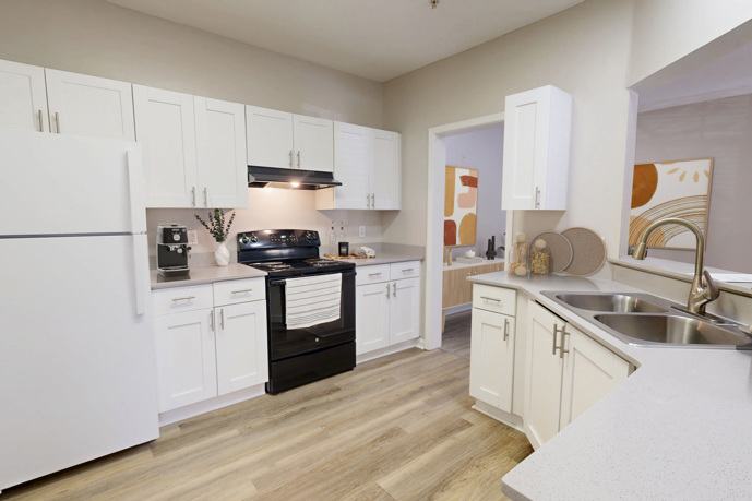 A kitchen at Sugar Mill apartments with a white refrigerator, microwave, and two chairs.